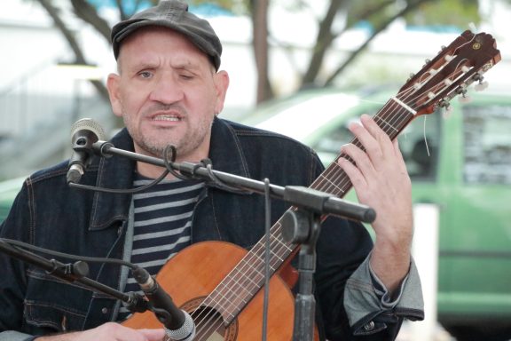 Fred P. Lohr ist mit seiner Gitarre zu sehen. Vor ihm stehen zwei Mikrophone für Gesang und Gitarre. Fred performt draußen.